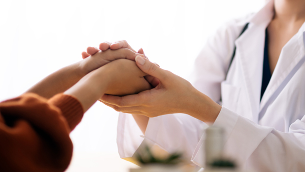 Nurse in white cloak holding patients hand across table